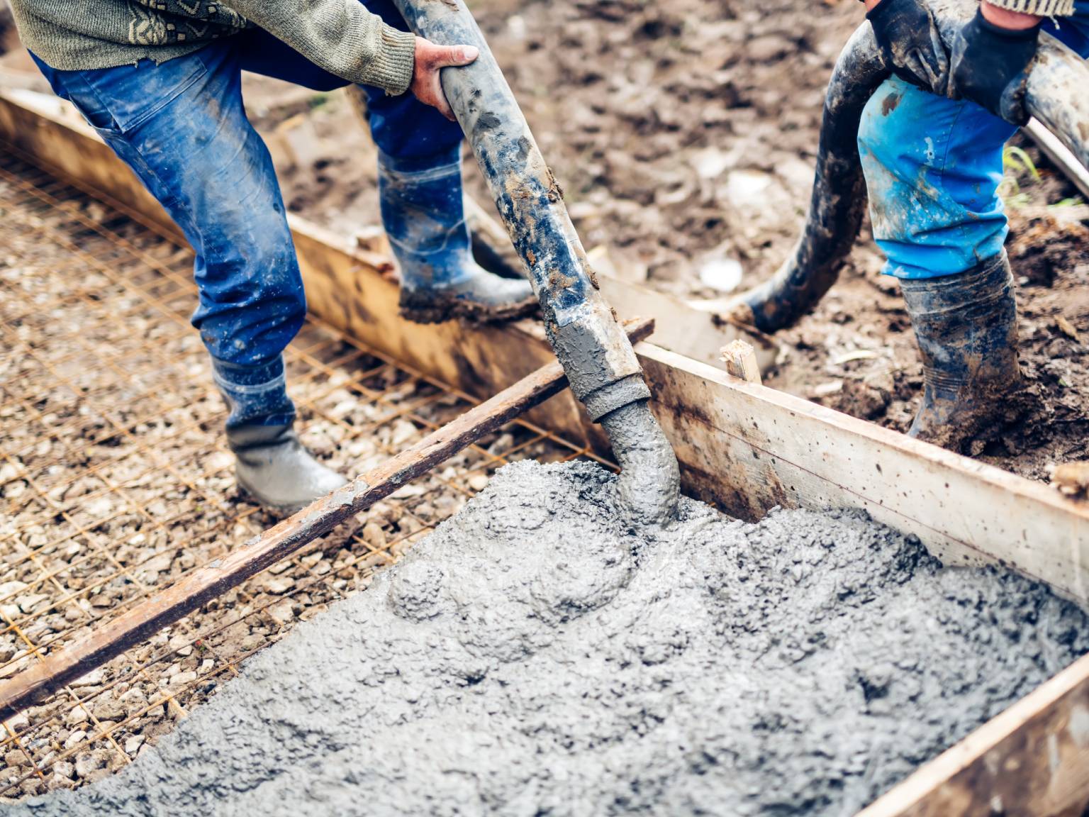 Turnare beton proaspăt într-o fundație cu ajutorul unei pompe, lucrători care nivelează și direcționează materialul pentru construcția unui proiect.